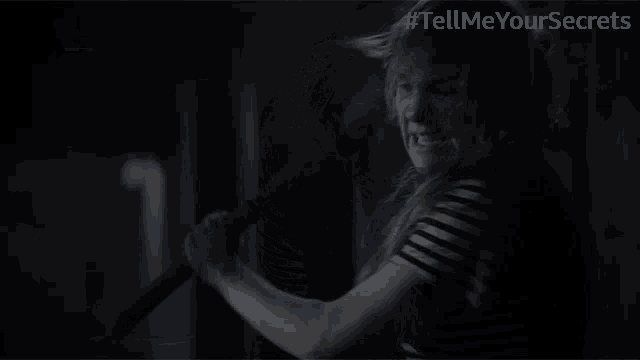 a woman in a striped shirt is holding an axe in a dark room with # tellmeyoursecrets written on the bottom right