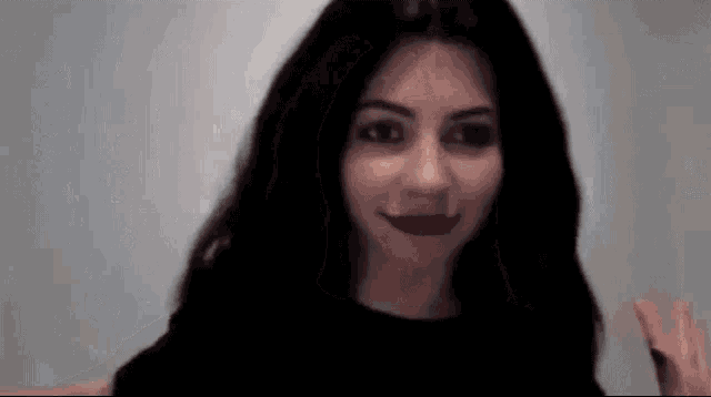 a woman with long black hair and red lipstick is smiling and waving .