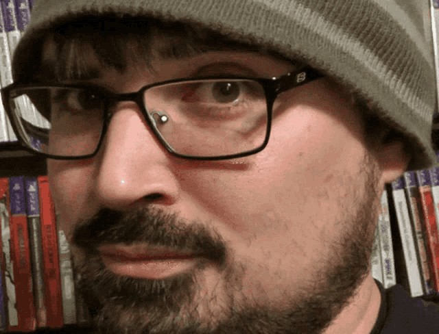 a man wearing glasses and a beanie is standing in front of a shelf full of ps4 games