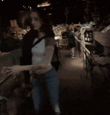 a woman in a crop top and jeans stands in a dark room with a sign that says ' a ' on it