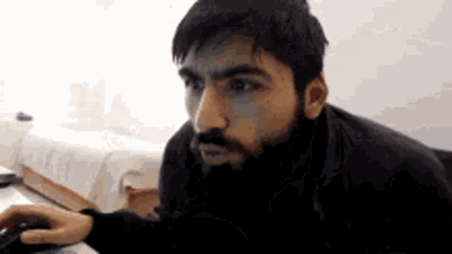 a man with a beard is using a computer mouse and looking at the camera .