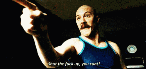 a man with a mustache and a blue tank top is saying shut the fuck up you cunt