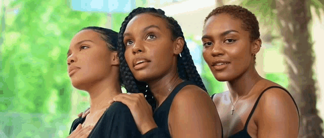 three women are standing next to each other in a park .