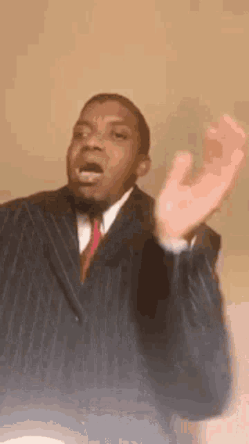 a man in a suit and tie is making a funny face while standing in front of a wall .