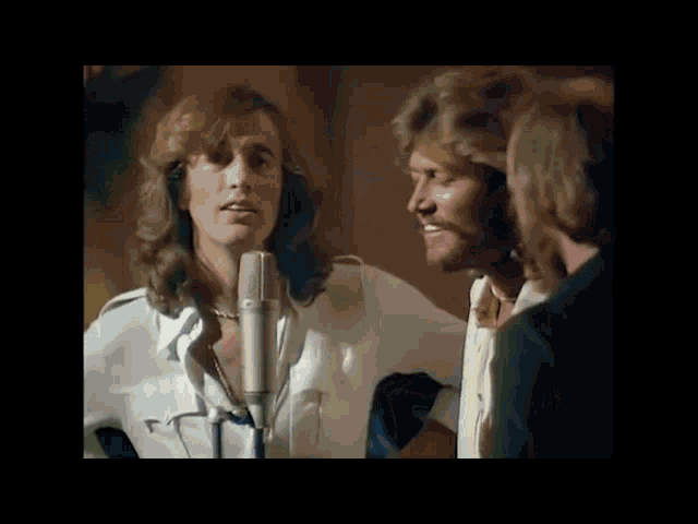 a woman is singing into a microphone while two men are standing behind her .