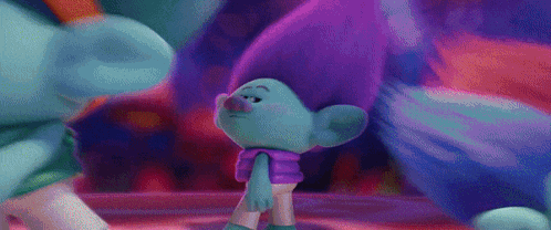a troll with purple hair is standing next to a blue troll in a room .
