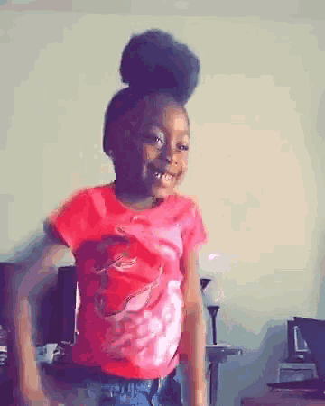 a little girl in a red shirt is dancing in a living room and smiling .