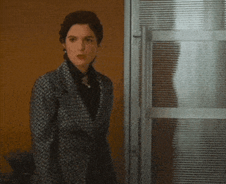 a woman in a black and white suit is standing in front of a glass door .