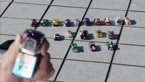 a person is holding a remote control in front of a group of toy cars