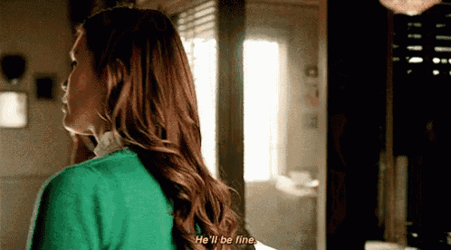 a woman in a green sweater is standing in a room and talking to someone .