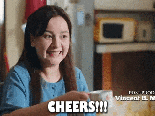 a woman in a blue shirt is holding a cup of coffee and cheers