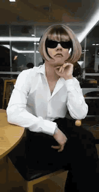 a woman in a white shirt and sunglasses is sitting at a table