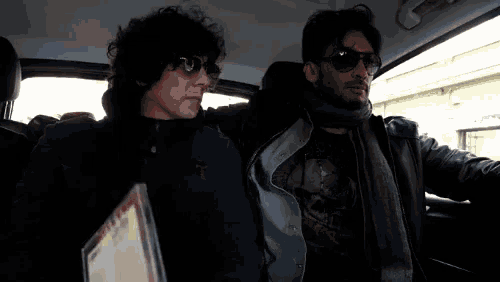 two men are sitting in a car with one wearing sunglasses and holding a menu