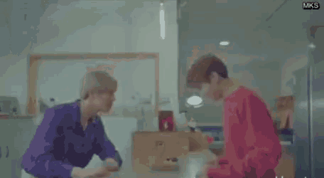 two men are standing next to each other in a kitchen and talking to each other .