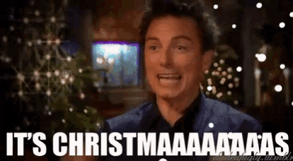 a man says it 's christmas while standing in front of a christmas tree