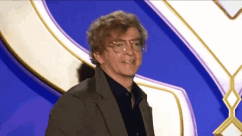 a man wearing glasses and a suit is standing in front of a blue background