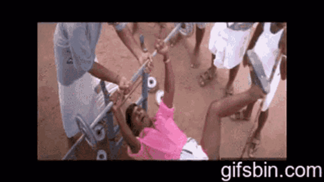 a man in a pink shirt is doing a pull up on a bar while a group of people watch .