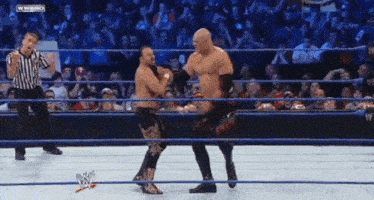 two wrestlers are fighting in a wrestling ring with a referee in the background