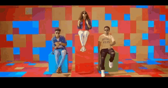 a woman is sitting on a red box next to two men .