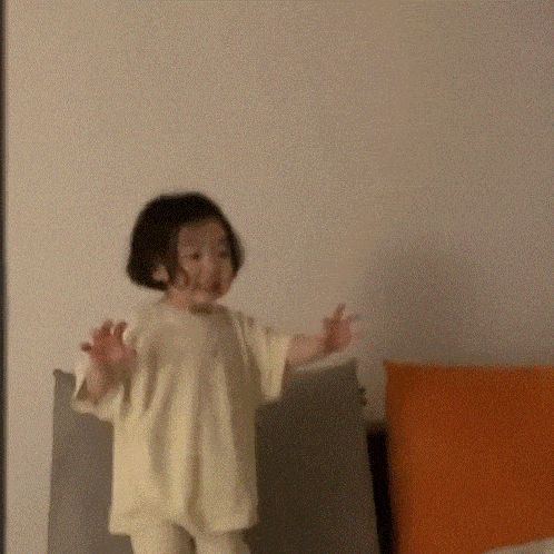 a little girl is standing in a room with her arms outstretched and looking at the camera .