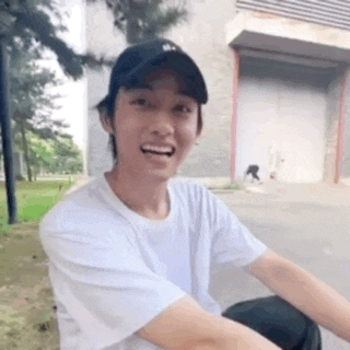 a young man wearing a white t-shirt and a black hat is smiling while riding a motorcycle .