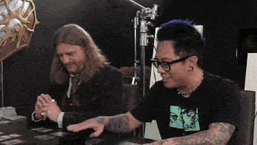 two men sitting at a table with one wearing a t-shirt with a picture of a man on it