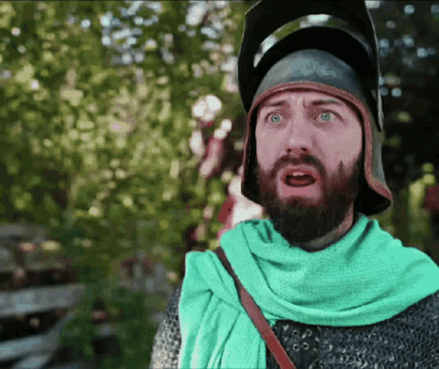 a man with a beard wearing a helmet and a green scarf has a surprised look on his face