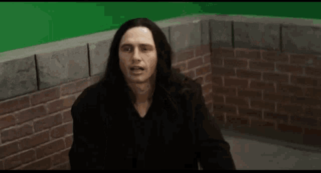 a man with long hair is sitting in front of a brick wall and the words it 's human behavior are above him