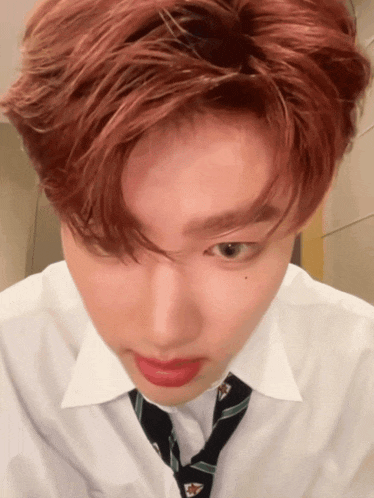 a young man with red hair wearing a white shirt and tie looks at the camera