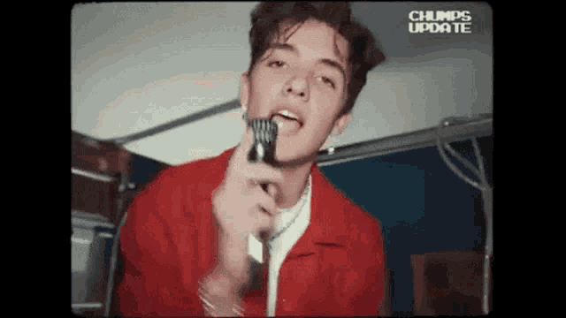 a young man in a red jacket is singing into a microphone with the words chumps update above him