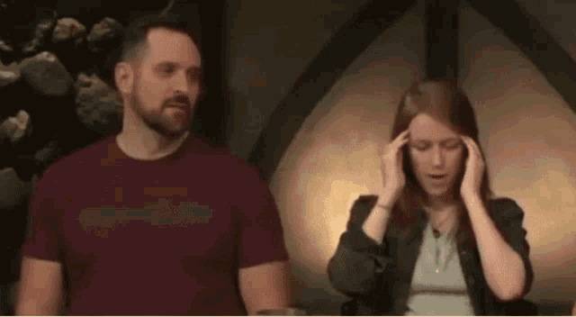 a man and a woman are standing next to each other in a room . the woman is holding her head .