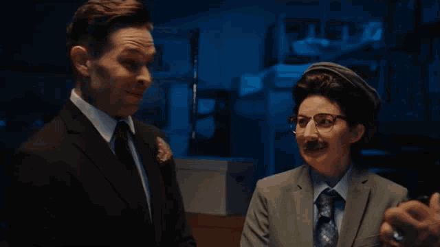 a man in a suit and tie is talking to a woman in glasses