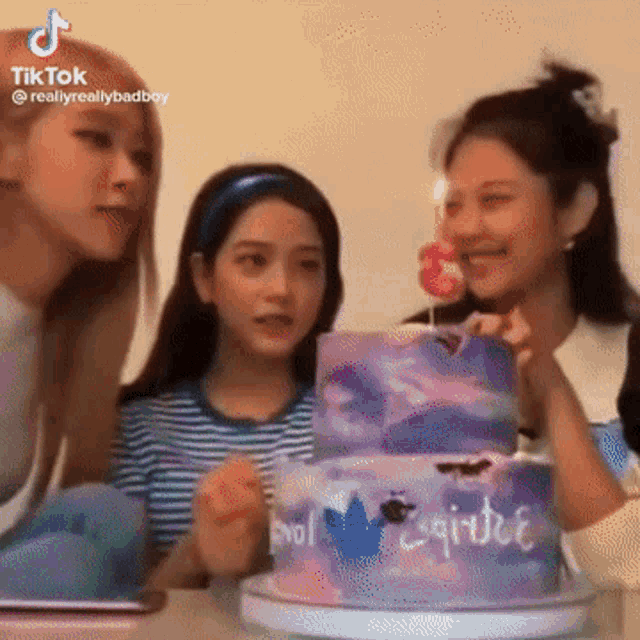 three girls are sitting at a table with a cake and a candle .
