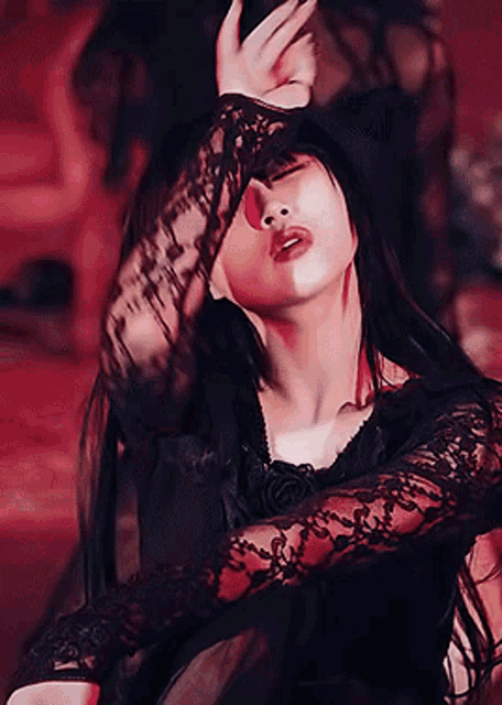 a woman in a black lace dress is covering her face with her hand .
