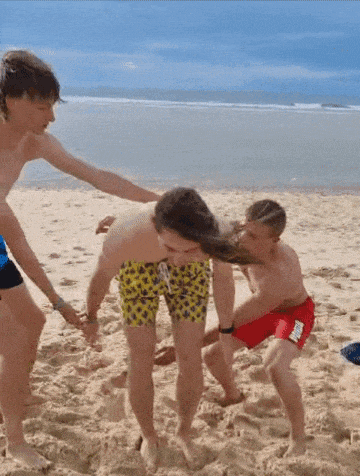 a group of boys are playing on the beach and one of them is wearing a pair of yellow shorts