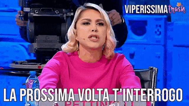 a woman in a pink sweater is sitting in front of a camera with the caption la prossima volta t ' interrogo