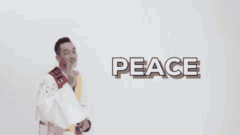 a man in a colorful outfit is standing in front of a wall with the word peace written on it .