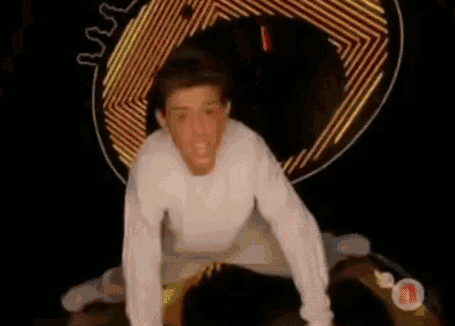 a man in a white sweater is kneeling down in front of a neon sign .