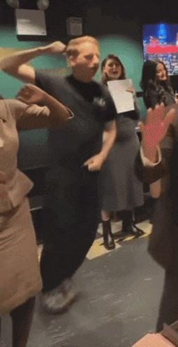 a man in a black shirt is dancing in a room with a sign that says ' nbc ' on it