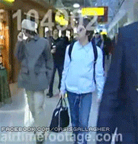 a group of people are walking down a hallway with a facebook.com/oasis gallagher advertisement in the corner