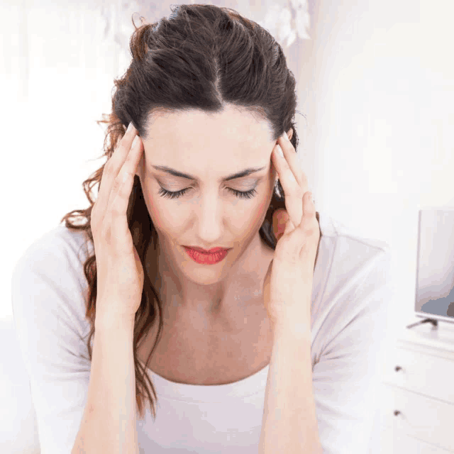 a woman with her eyes closed is holding her head in pain