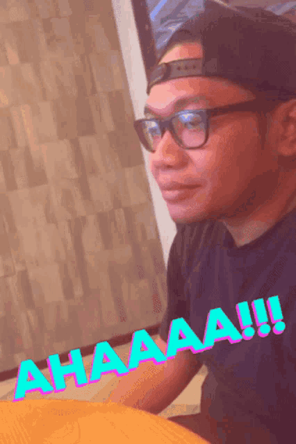 a man wearing glasses and a hat is sitting at a table with the word ahaaa written on the table
