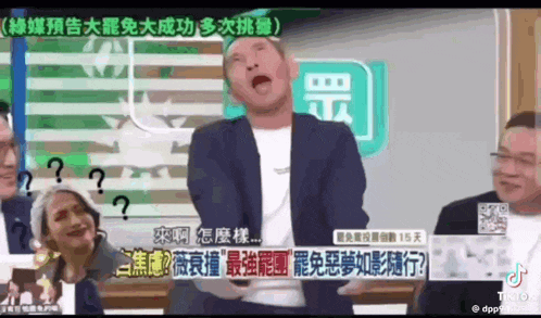 a man in a suit is making a funny face in front of a group of people in chinese .