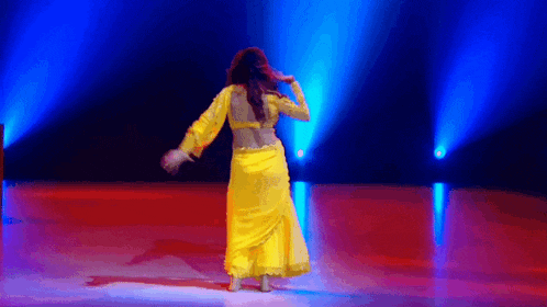 a woman in a yellow dress is dancing on a stage with blue lights behind her