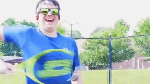 a man wearing sunglasses is holding a tennis racket and smiling .