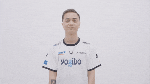a young man wearing a white yodo shirt points his finger at the camera