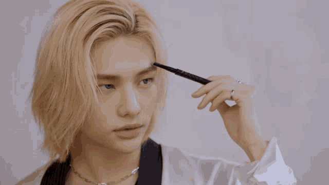 a man with blonde hair is applying eyeliner on his eyebrows