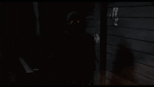a shadow of a person with red eyes is standing in the dark
