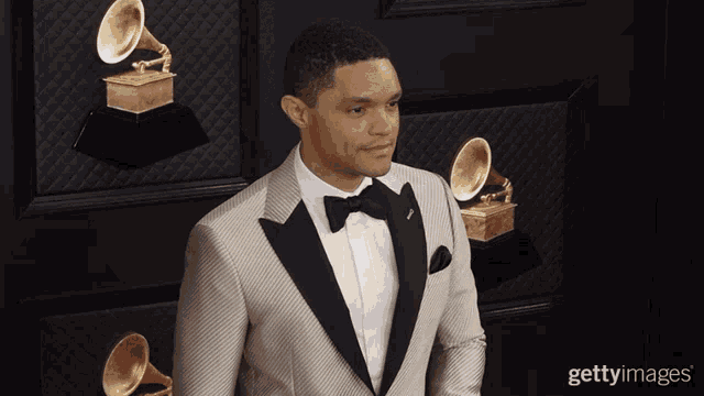 a man in a tuxedo and bow tie is standing in front of a wall of grammophones