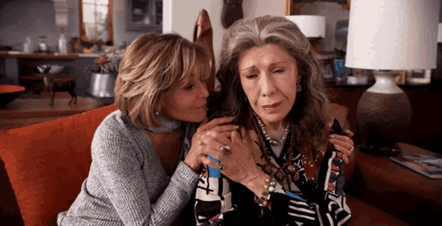 two women are sitting on a couch and one of them has a bracelet that says t on it